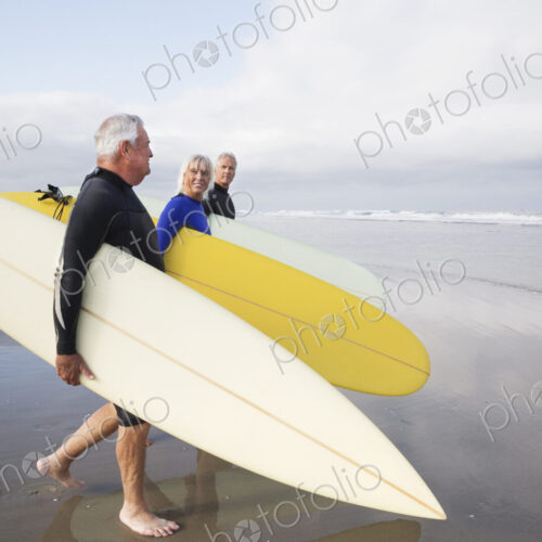 Senior woman and two senior men on a beach, wearing wetsuits and carrying surfboards. Senior woman and two senior men on a beach, wearing wetsuits and carrying surfboards.