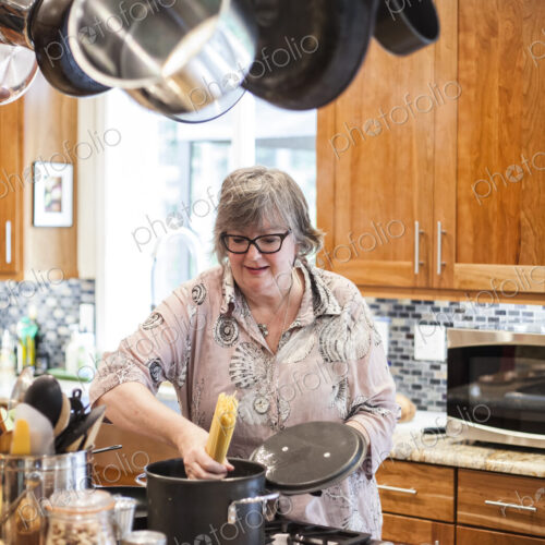 Senior woman checking to see if a pot of pasta is cooking correctly in a home kitchen.