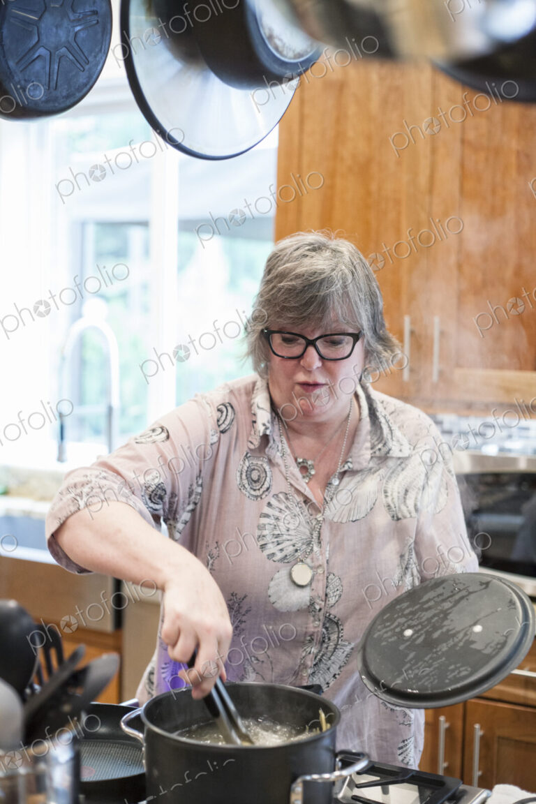 Senior woman checking to see if a pot of pasta is cooking correctly in a home kitchen.