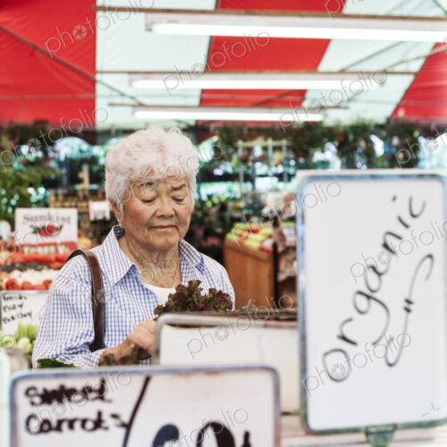 Senior woman standing at a stall in a fruit and vegetable market, looking at lettuce. Senior woman standing at a stall in a fruit and vegetable market, looking at lettuce.