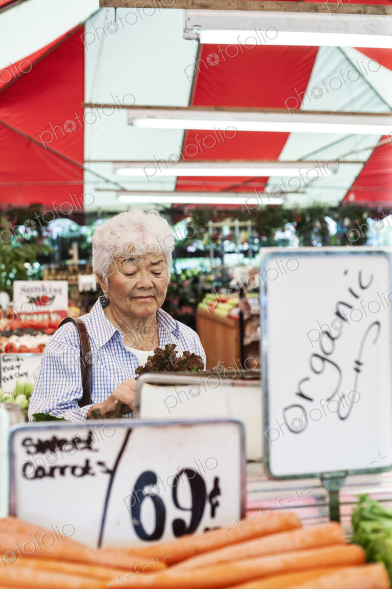 Senior woman standing at a stall in a fruit and vegetable market, looking at lettuce.