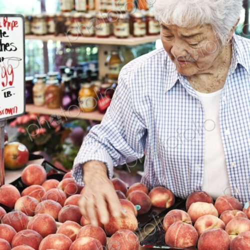 Senior woman standing at stall with fresh white peaches at a fruit and vegetable market.