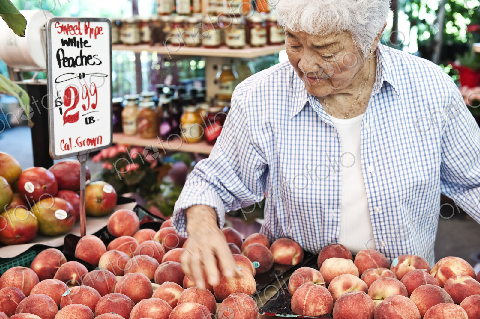 Senior woman standing at stall with fresh white peaches at a fruit and vegetable market.