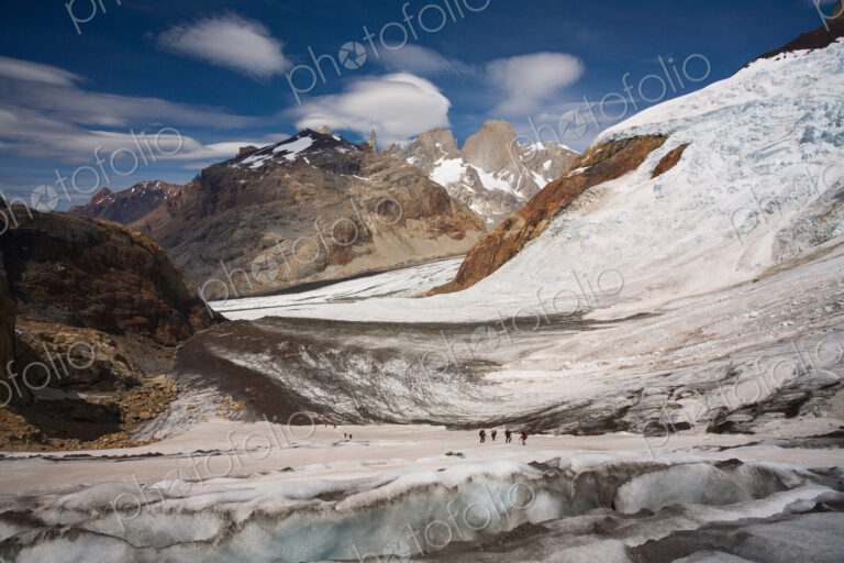 Several hikers on a glacier and Fitz Roy loom in the background. Los Glaciares…