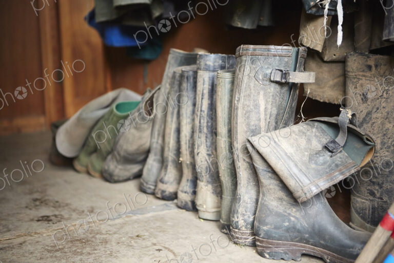 Several pairs of muddy wellington boots on a stone floor.