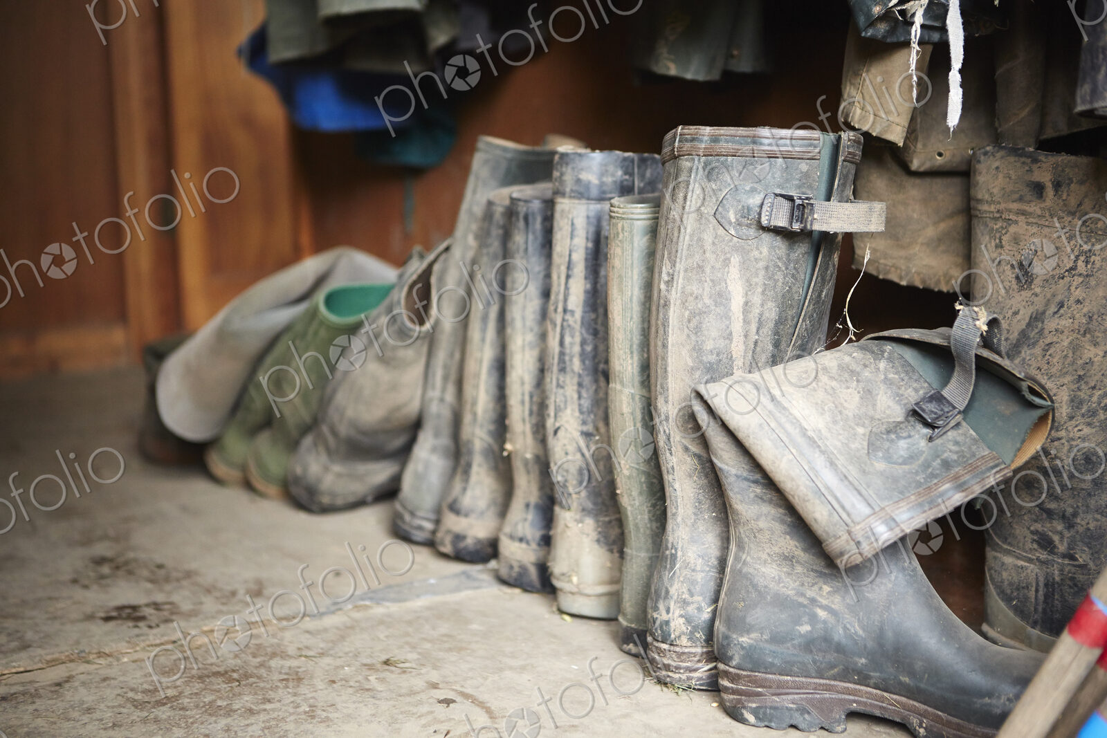 Several pairs of muddy wellington boots on a stone floor.