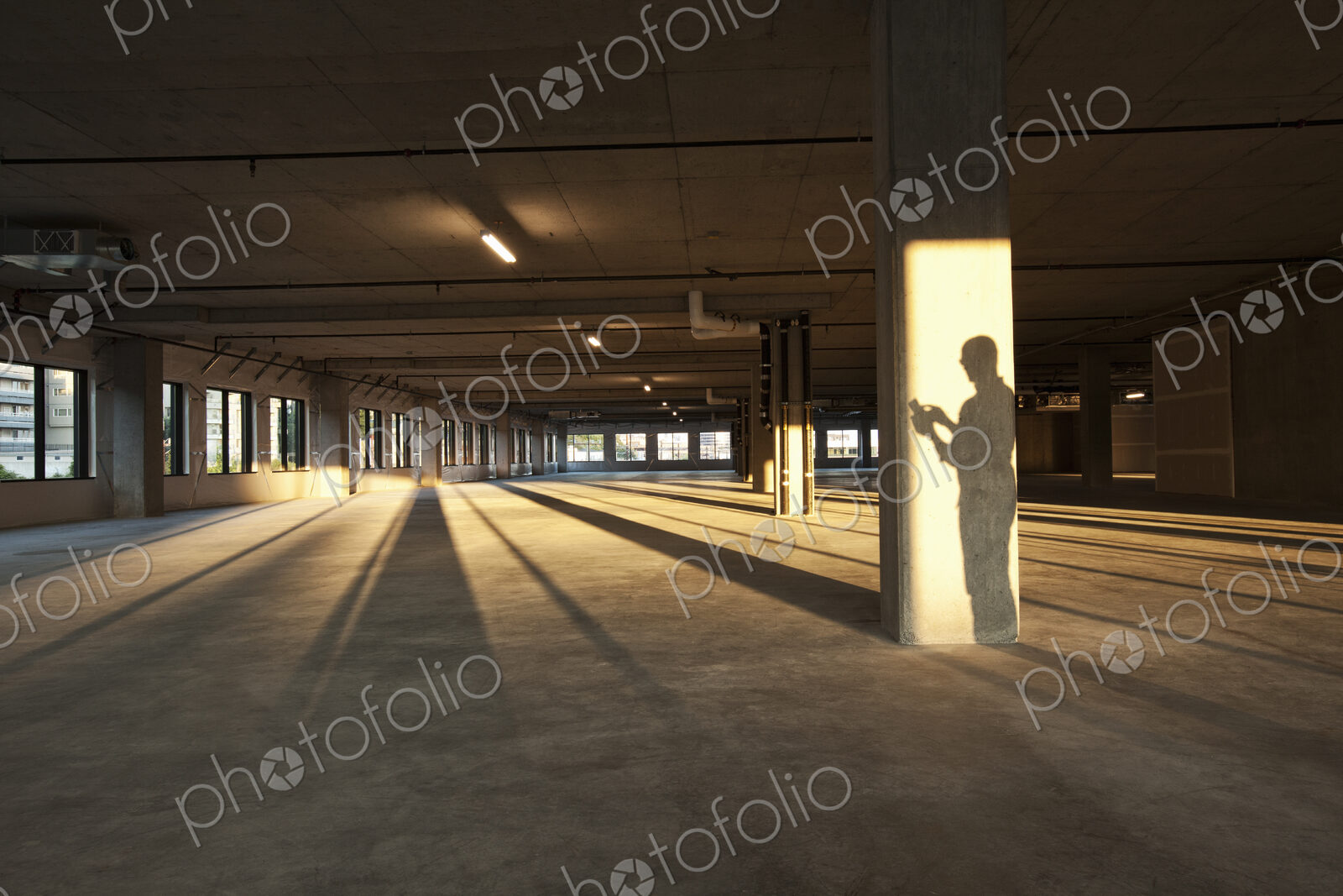 Shadow of a business man cast on a central post of a large empty raw office space.