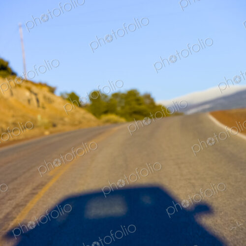 Shadow of a car on a two lane highway through the landscape.