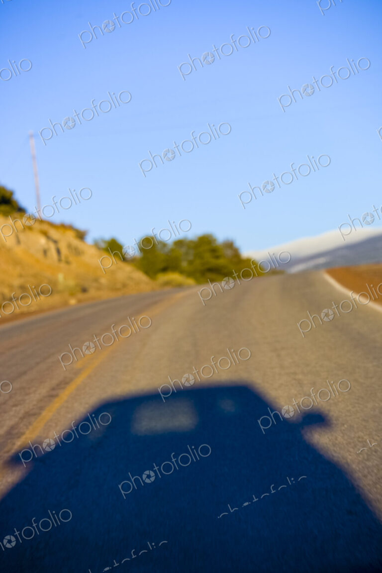 Shadow of a car on a two lane highway through the landscape.