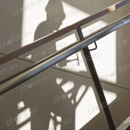 Shadow of a construction worker walking up stairs on wall with handrail.