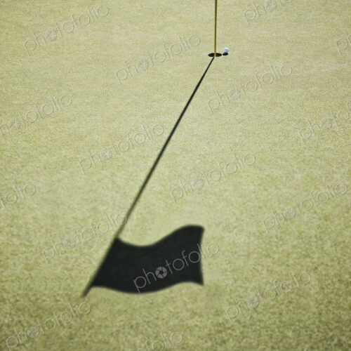 Shadow of a golf flag on the green of a golf course.