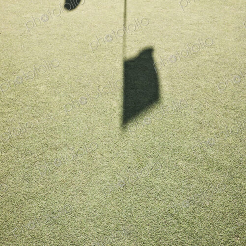 Shadow of a golfer and a flag on a golf green.