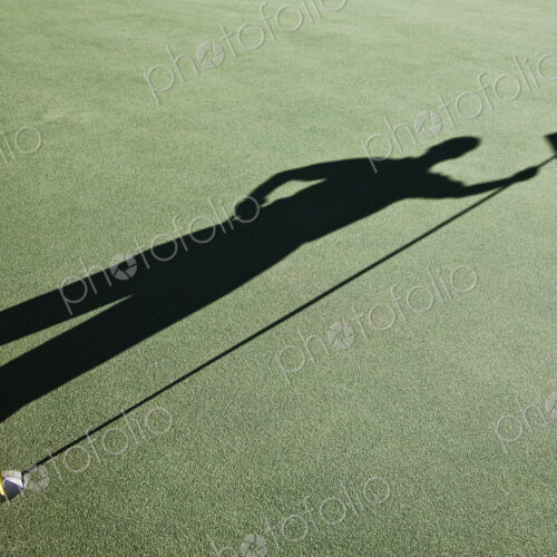 Shadow of golfers and the flag on a green of a golf course.