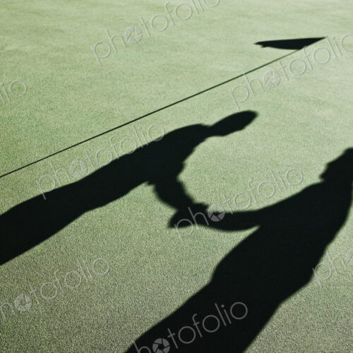 Shadow of golfers and the flag on a green of a golf course.