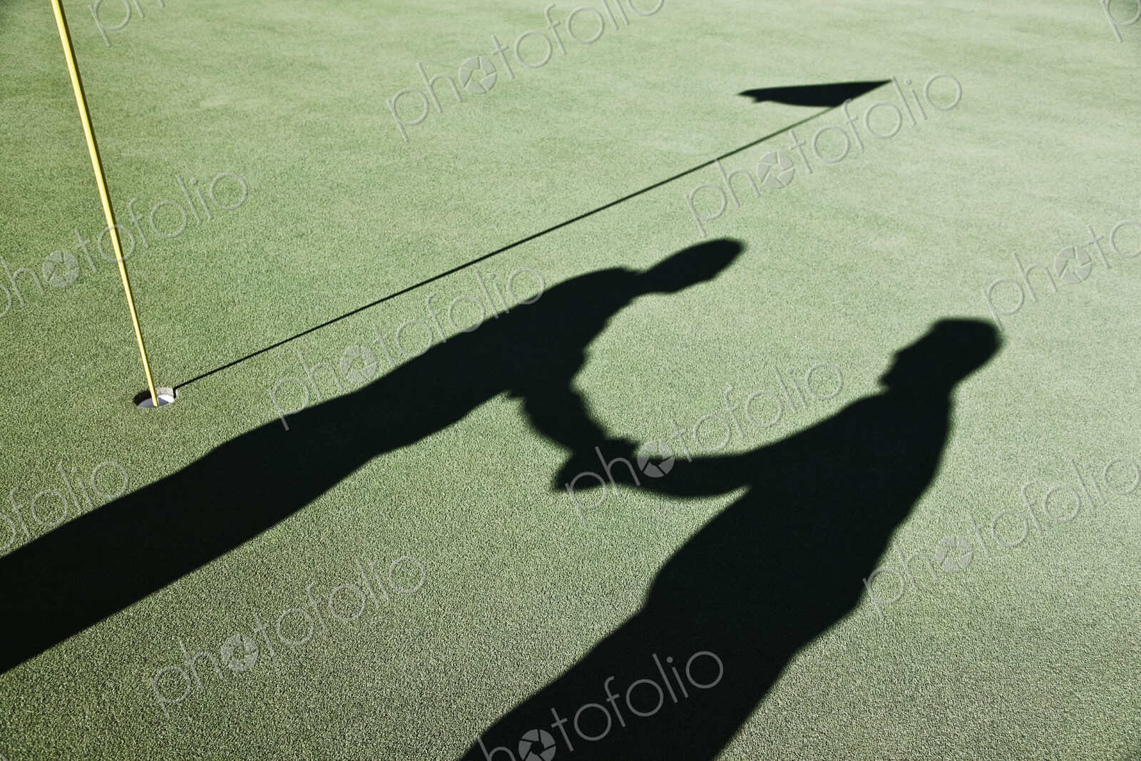 Shadow of golfers and the flag on a green of a golf course.