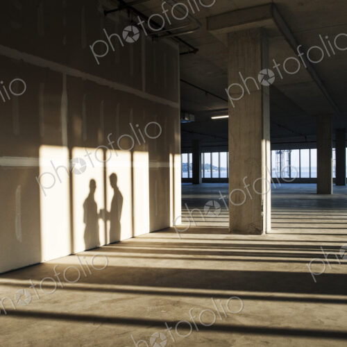 Shadows of business people cast on the sheet rock wall of a large empty raw office space. Shadows of business people cast on the sheet rock wall of a large empty raw office space.