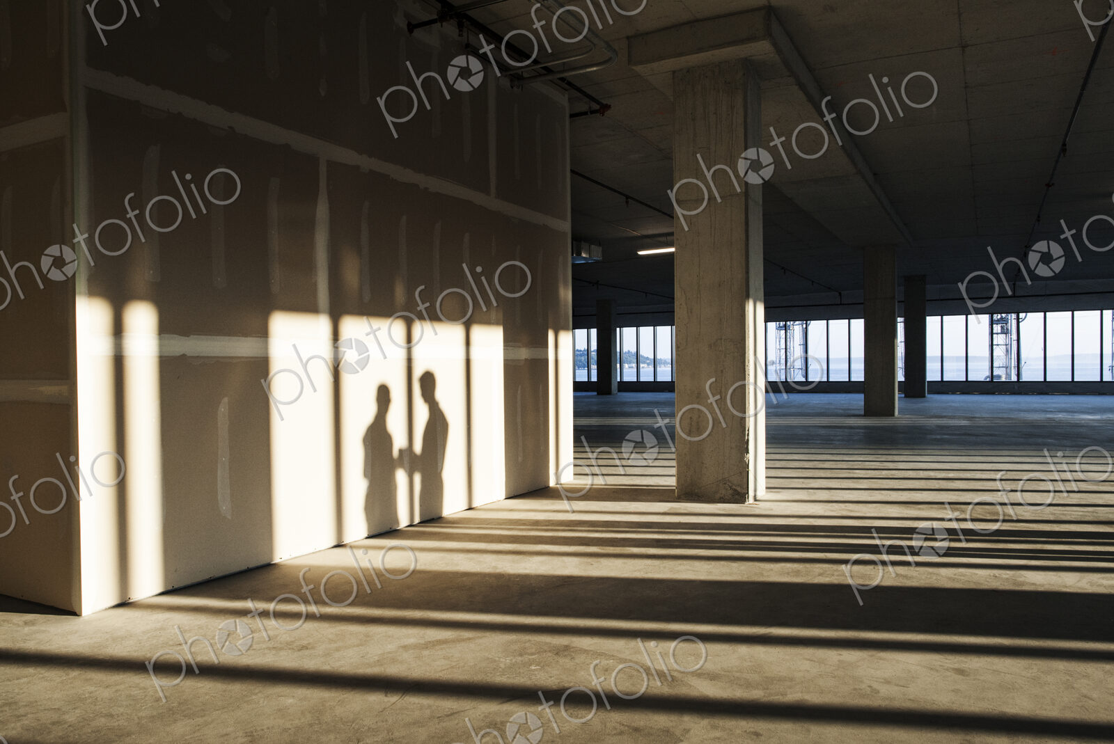 Shadows of business people cast on the sheet rock wall of a large empty raw office space.