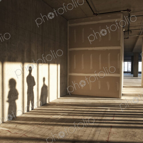 Shadows of business people cast on the sheet rock wall of a large empty raw office space.