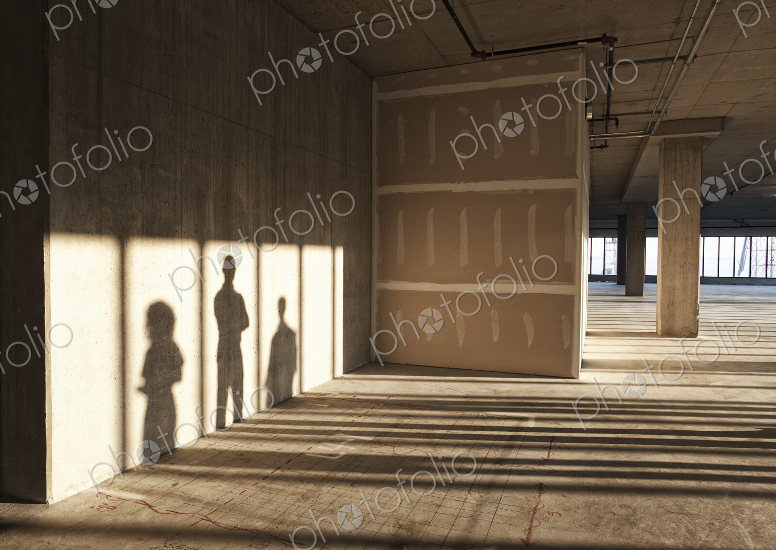 Shadows of business people cast on the sheet rock wall of a large empty raw office space.