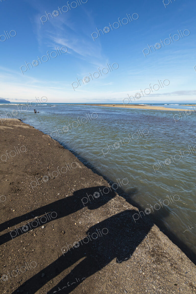 Shadows of two people on beach sand alongside the Elwha River, Port Angeles, WA USA
