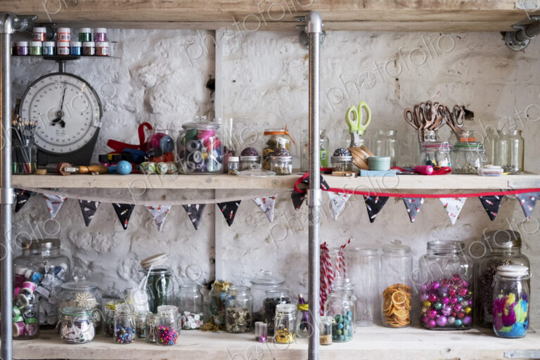Shelves, stock of scissors and colourful beads in glass jars, for sewing and craft.