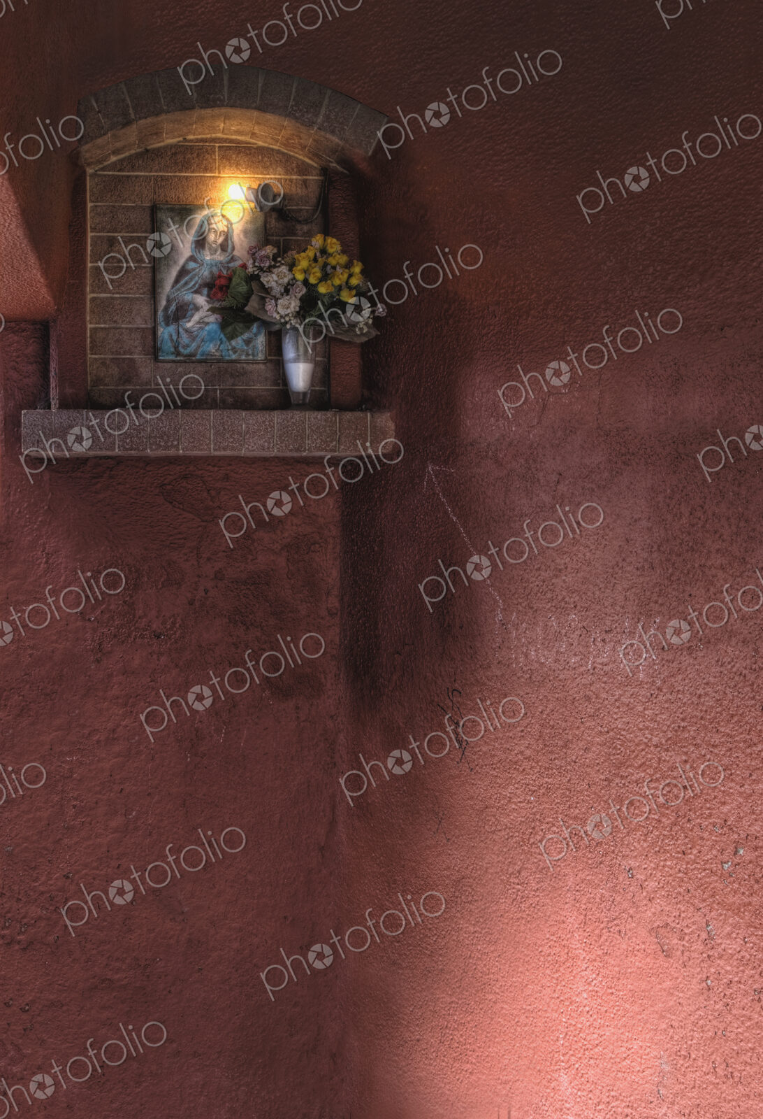 Shrine to the Virgin Mary on wall lit up at night.