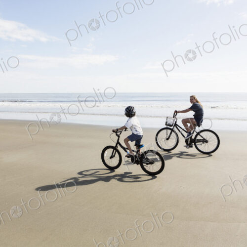 Siblings, a boy and girl cycling on a beach.