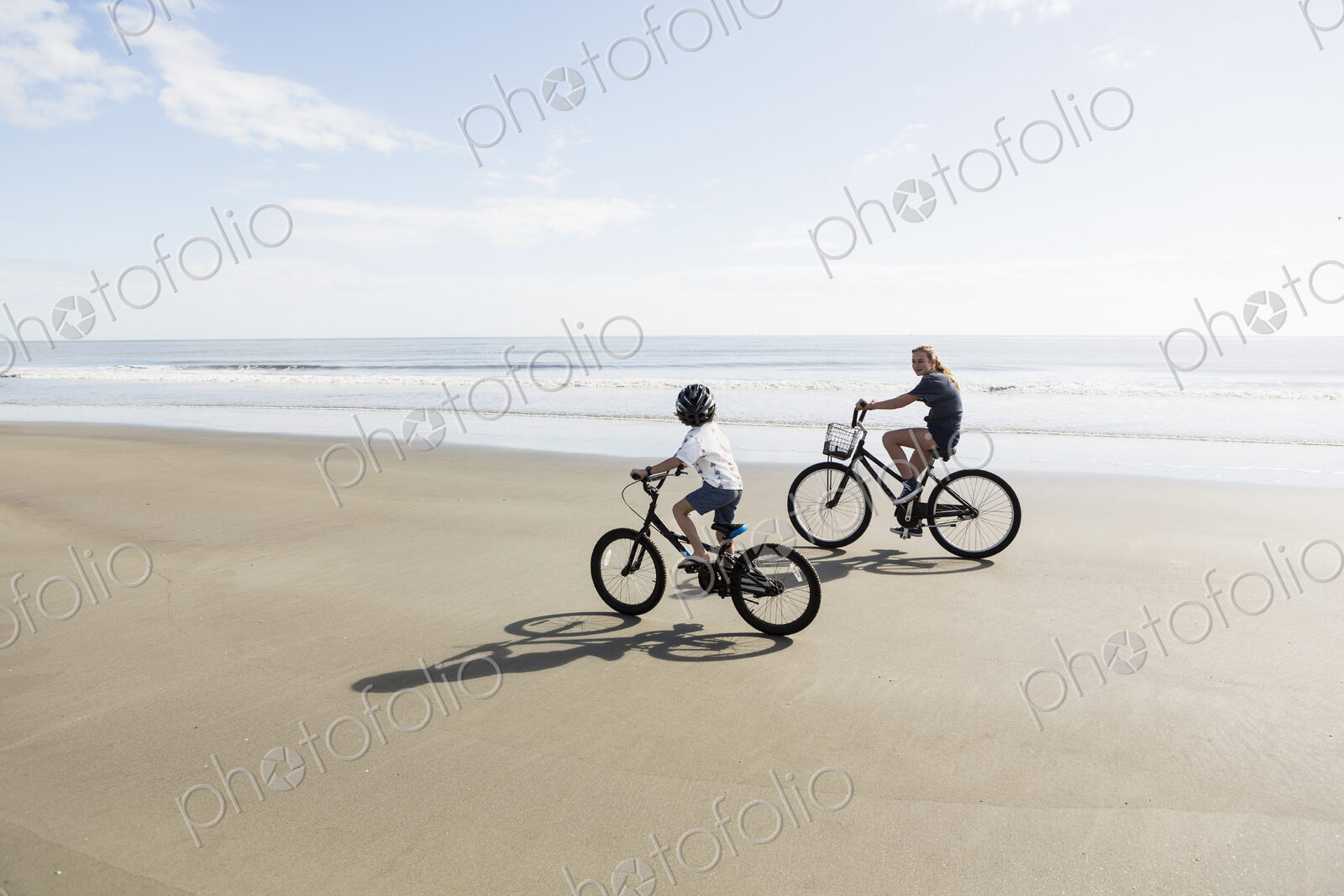 Siblings, a boy and girl cycling on a beach.