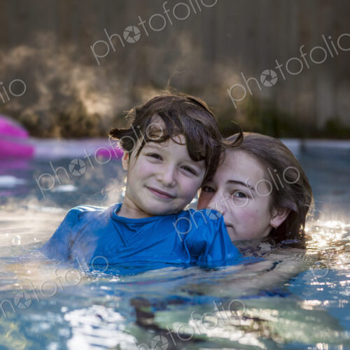 Siblings playing in pool in early morning light Siblings playing in pool in early morning light