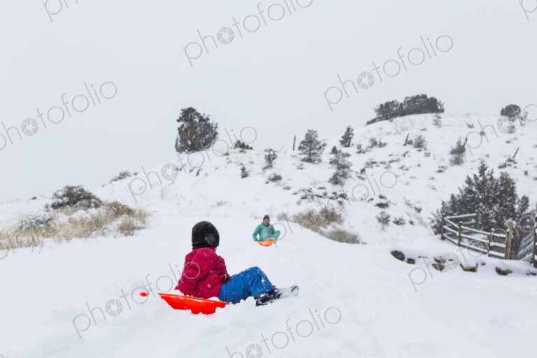 Siblings sledding down hill