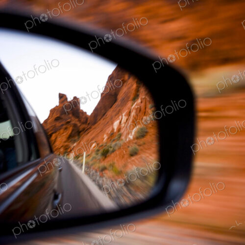 Side Mirror Reflection of the road already travelled and the steep red cliffs of… Side Mirror Reflection of the road already travelled and the steep red cliffs of…