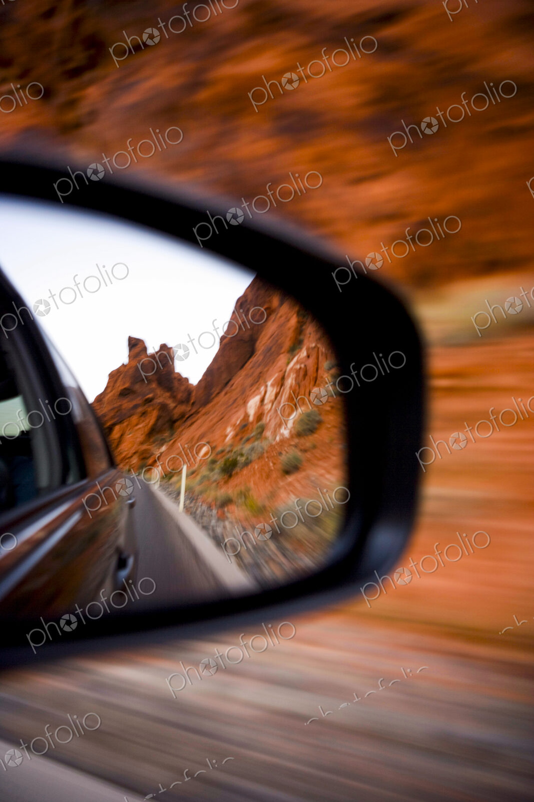 Side Mirror Reflection of the road already travelled and the steep red cliffs of…