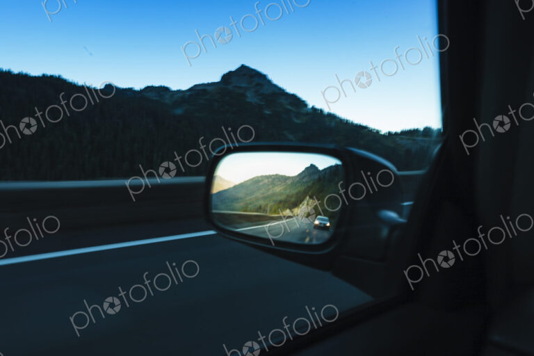Side mirror of a car passing through mountainous landscape, the view ahead and behind.
