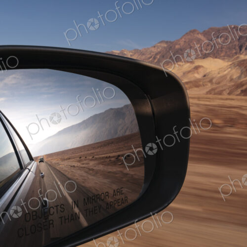 Side mirror view of a car, view of the road behind in a desert national park landscape.