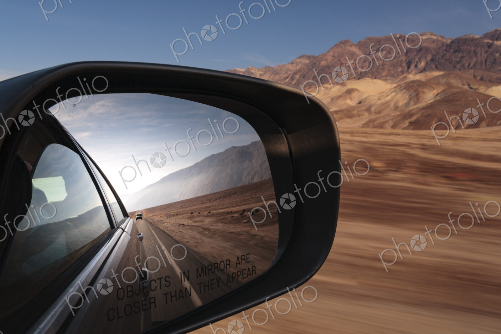 Side mirror view of a car, view of the road behind in a desert national park landscape.