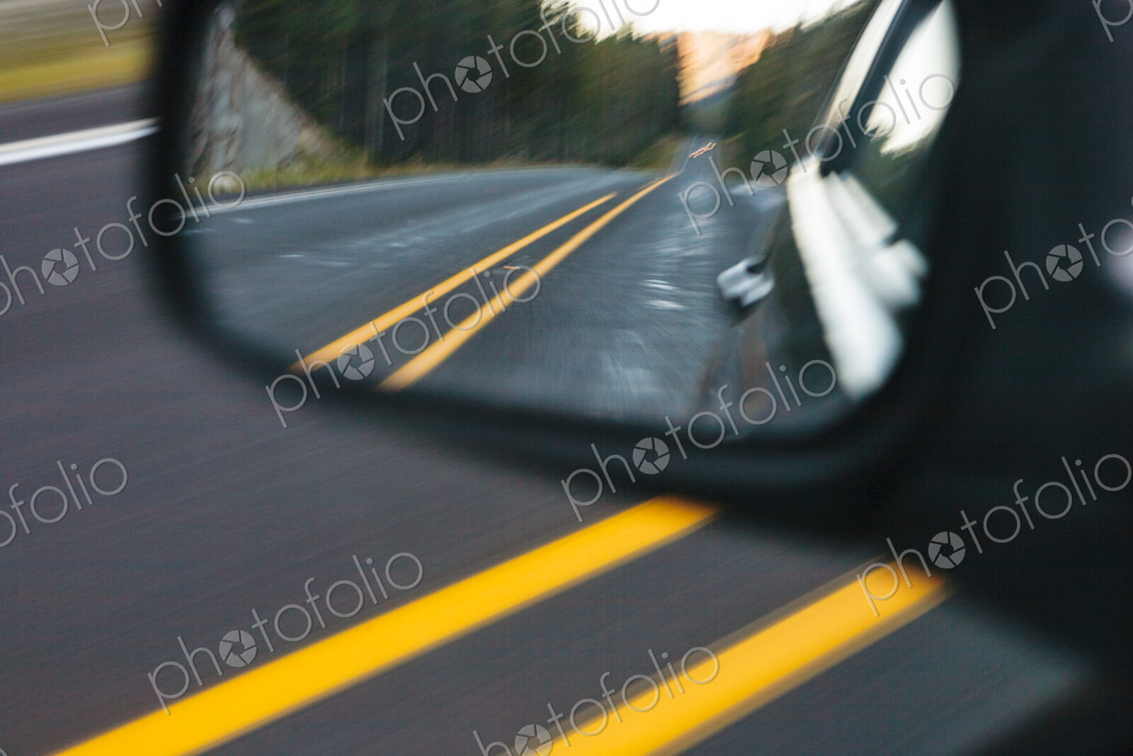 Side mirror view of a mountain highway, the road behind the car.