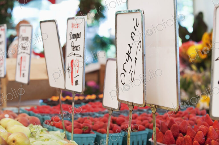 Signs and organic produce at vegetable stall in market.