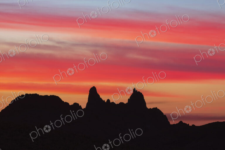 Silhouette of Mule Ears, two peaks at sunrise below a glowing sky, Big Bend National Park.