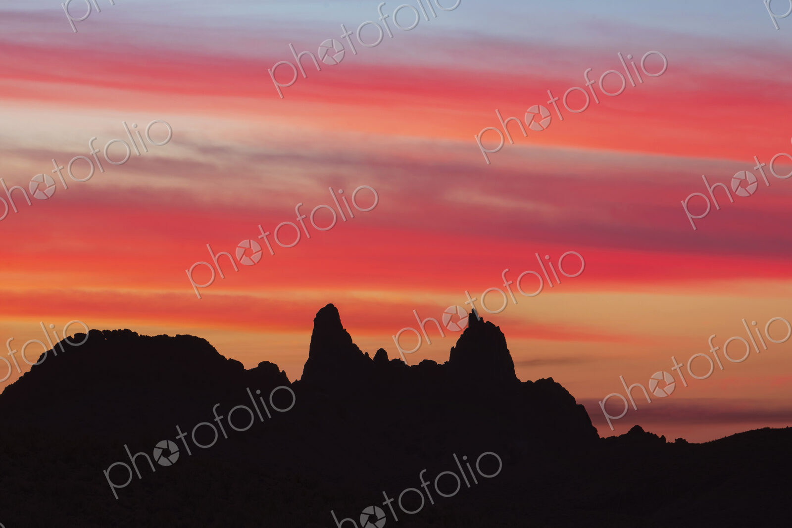 Silhouette of Mule Ears, two peaks at sunrise below a glowing sky, Big Bend National Park.