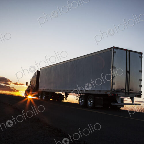 Silhouette of a commercial truck driving on a highway at sunset.