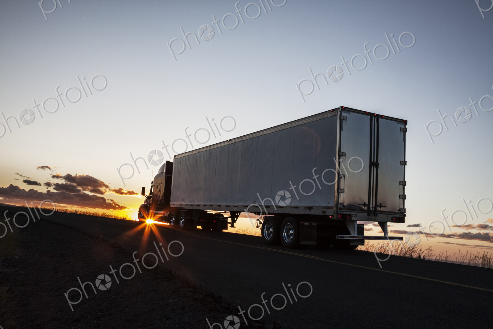 Silhouette of a commercial truck driving on a highway at sunset.