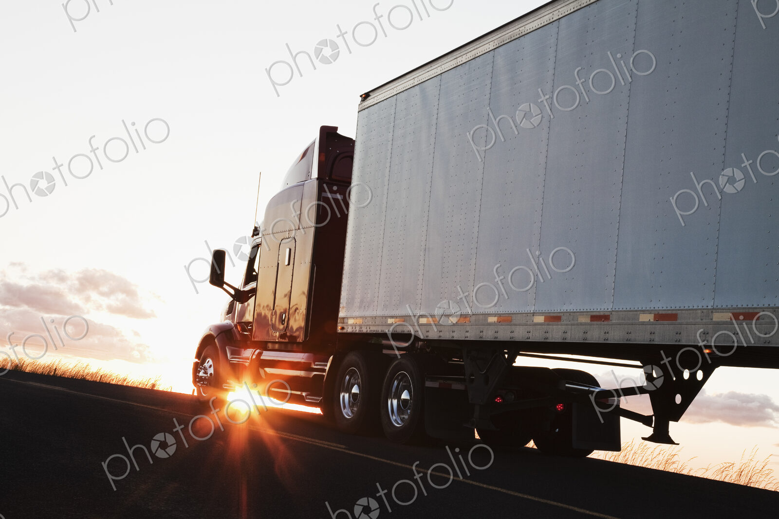 Silhouette of a commercial truck driving on a highway at sunset.