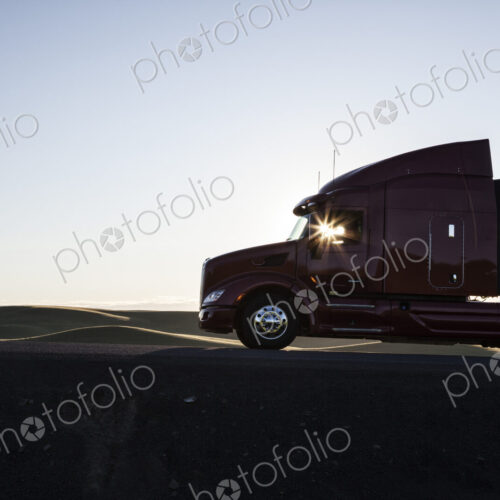 Silhouette of a commercial truck driving on a highway at sunset.