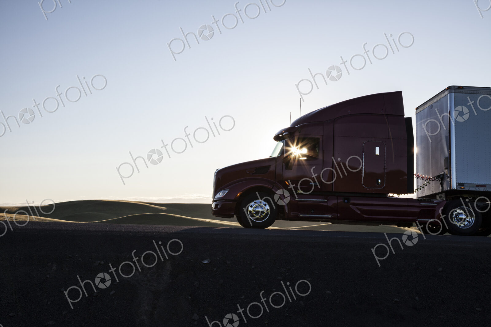 Silhouette of a commercial truck driving on a highway at sunset.