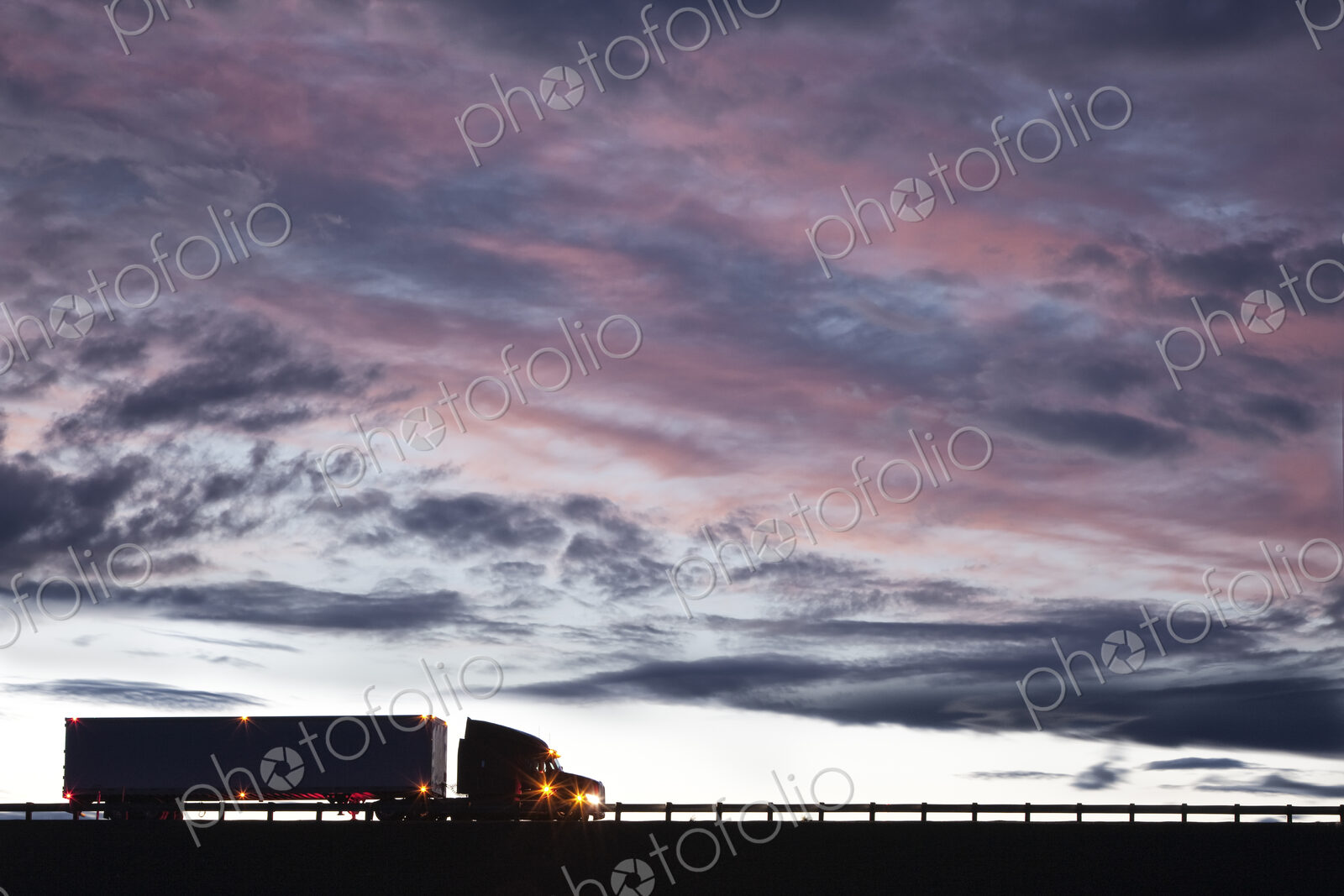 Silhouette of a commercial truck driving on a highway at sunset.