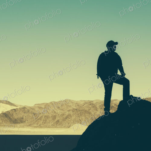 Silhouette of a hiker wearing a backpack, pausing to take in view of mountains and…