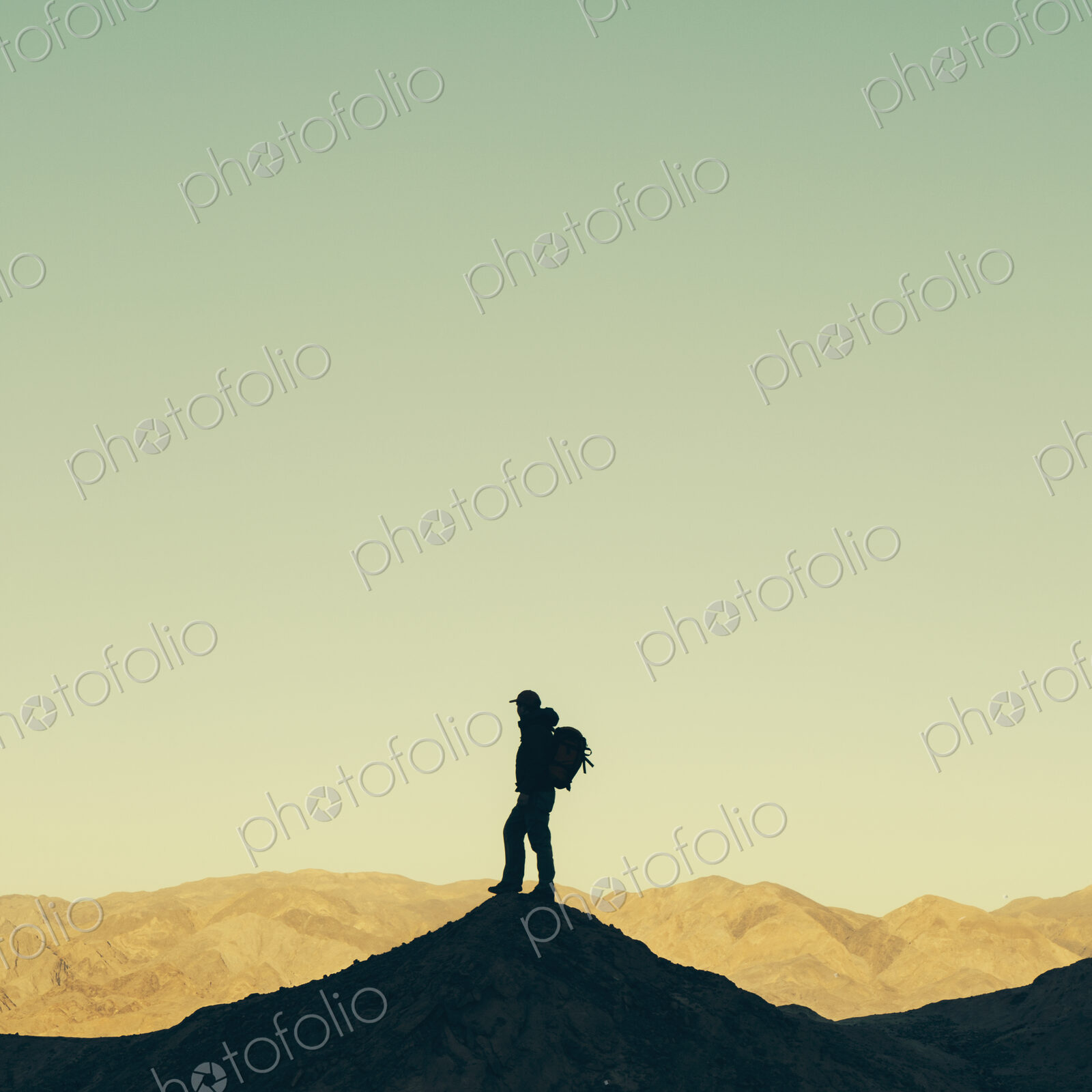 Silhouette of a male hiker wearing a backpack and standing on a hilltop in Death…