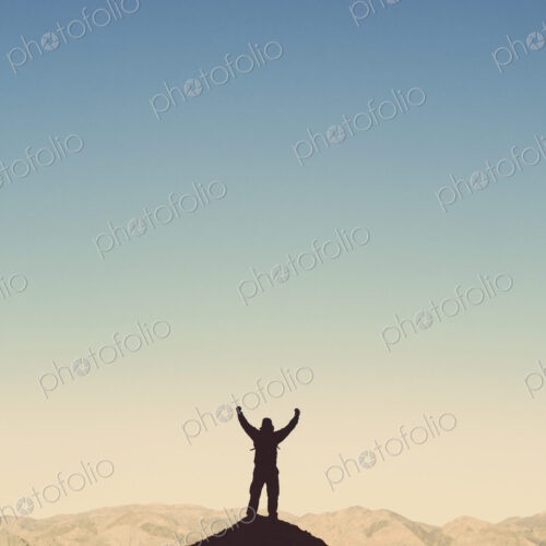 Silhouette of a male hiker wearing a backpack and standing on a hilltop in Death…