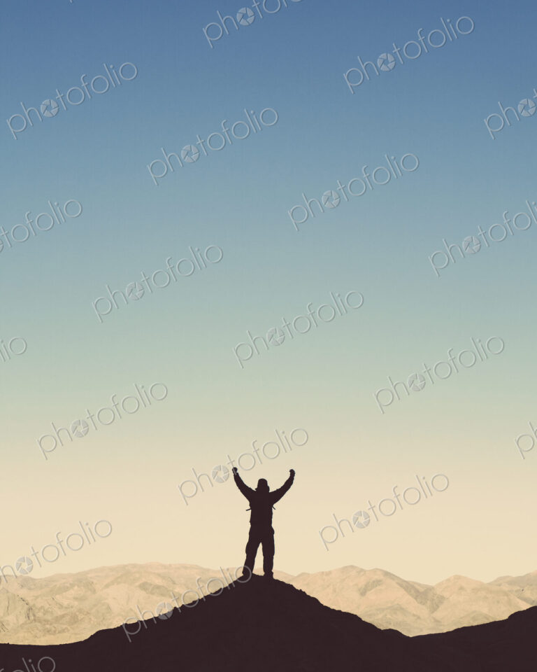 Silhouette of a male hiker wearing a backpack and standing on a hilltop in Death…