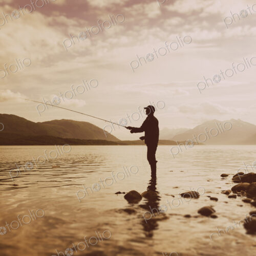 Silhouette of a man flyfishing in calm waters on the Waschusett inlet in Glacier Bay…